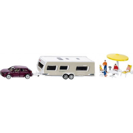 Spielzeugauto zieht Wohnwagen an, daneben sitzen Miniaturfiguren unter einem gelben Sonnenschirm.