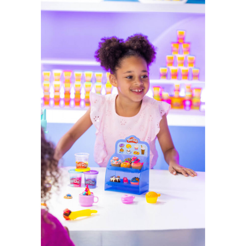 Mädchen spielt lächelnd mit Play-Doh und Spielzeugdesserts an einem Tisch in gut beleuchtetem Raum. Mädchen spielt lächelnd mit Play-Doh und Spielzeugdesserts an einem Tisch in gut beleuchtetem Raum.