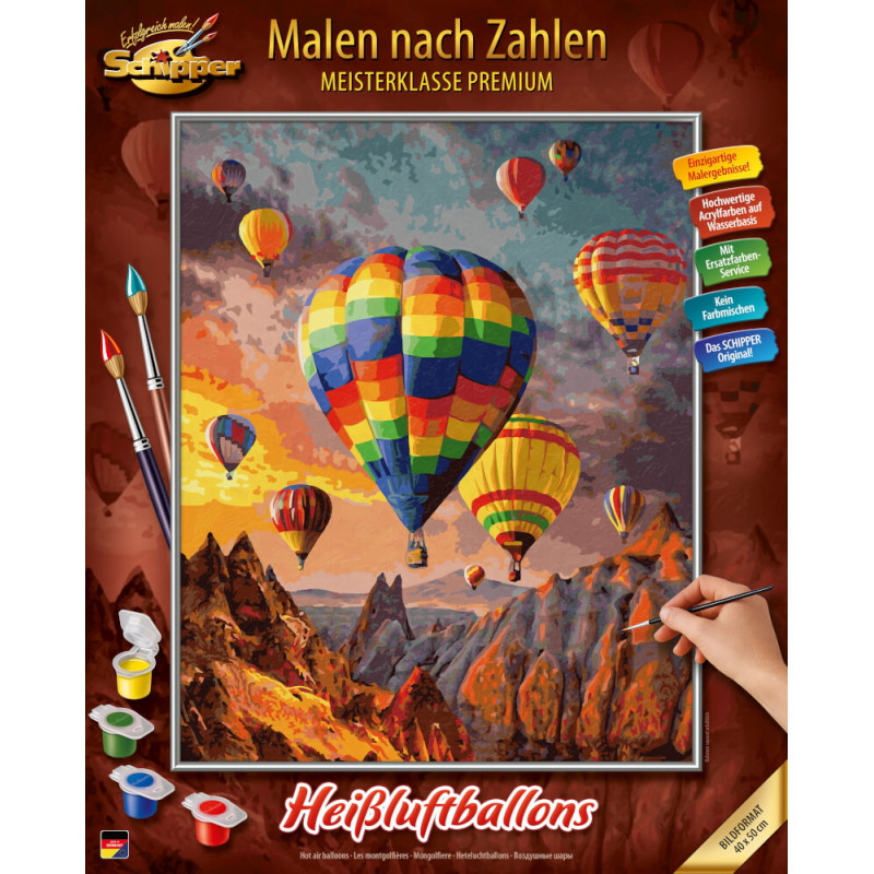 Eine Hand malt eine bunte Heißluftballonszene über Bergen, unten sind Farbtöpfe und Pinsel zu sehen.