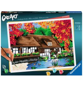 Malkasten mit Motiv: Eine Hand malt ein Haus am Teich, umgeben von bunten Herbstbäumen.