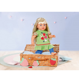 Eine blonde Puppe im grünen Erdbeerkleid sitzt in einem Korb auf einem pastellfarbenen Teppich.