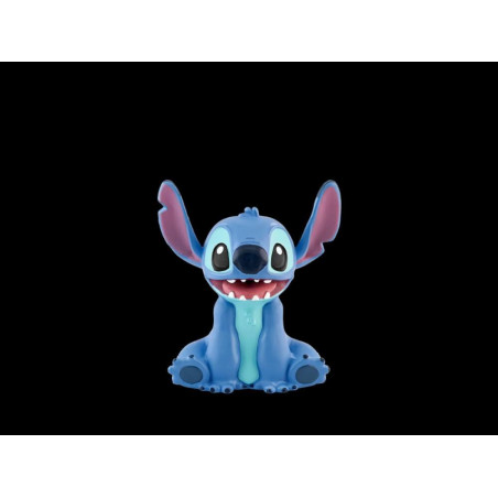 Ein blauer Cartoon-Alien mit großen Ohren und breitem Lächeln sitzt vor schwarzem Hintergrund.