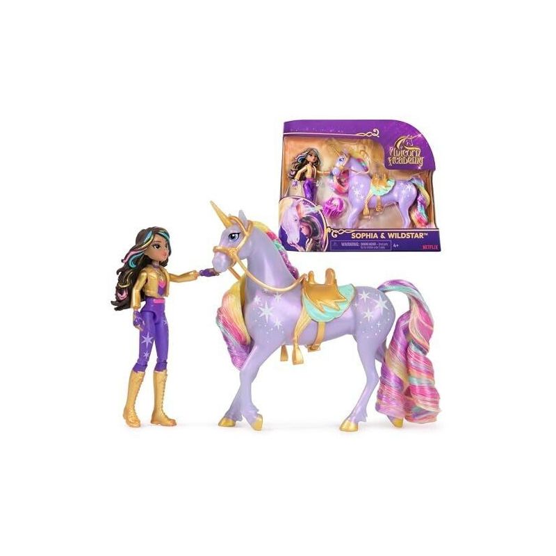 Puppe im lila-goldenen Outfit steht neben einem Einhorn mit bunter Mähne und Flügeln, Karton im Hintergrund. Puppe im lila-goldenen Outfit steht neben einem Einhorn mit bunter Mähne und Flügeln, Karton im Hintergrund.
