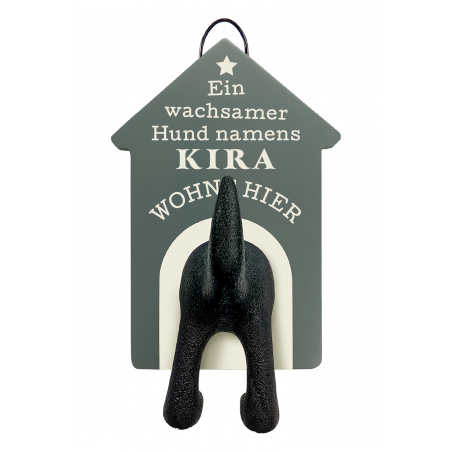 Aus einem Schild mit Ein wachsamer Hund namens Kira wohnt hier ragen Hundeschwanz und Hinterbeine hervor.
