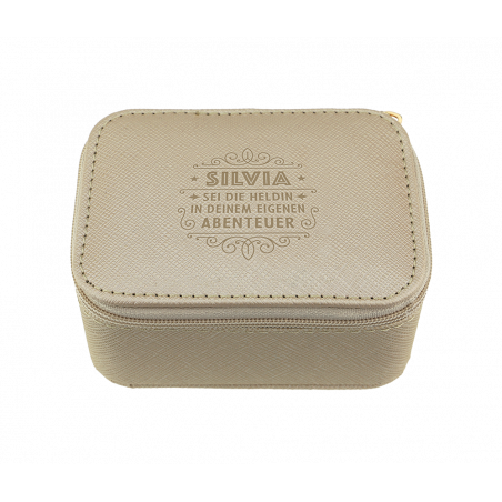 Beiges Etui mit Reißverschluss und geprägtem Text SILVIA SEI DIE HELDIN IN DEINEM EIGENEN ABENTEUER auf dem Deckel.