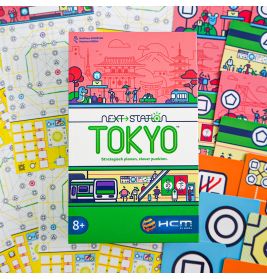 Die Next Station: Tokyo-Spielschachtel liegt auf bunten Spielbögen und Komponenten des Brettspiels.