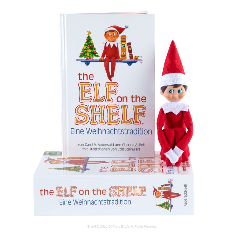 Elf on the Shelf-Puppe sitzt neben zwei Exemplaren des Buches The Elf on the Shelf: Eine Weihnachtstradition. Elf on the Shelf-Puppe sitzt neben zwei Exemplaren des Buches The Elf on the Shelf: Eine Weihnachtstradition.
