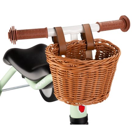 Nahaufnahme eines Kinderfahrrad-Lenkers mit braunem Weidenkorb, der vor dem Sitz befestigt ist.