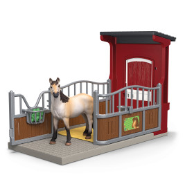 Ein Spielzeugpferd steht in einem kleinen, umzäunten Stall mit roter Tür und grünem Futtereimer an der Seite.