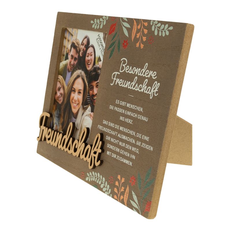 Holzrahmen mit deutschem Text, Blumenmustern und einem Gruppenfoto lachender Freunde.