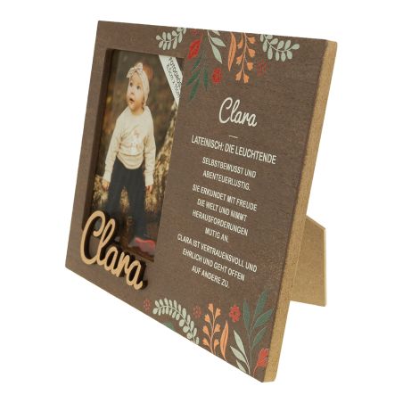 Holzrahmen mit Blumenmuster, Babyfoto und Name "Clara" - daneben eine deutschsprachige Beschreibung.
