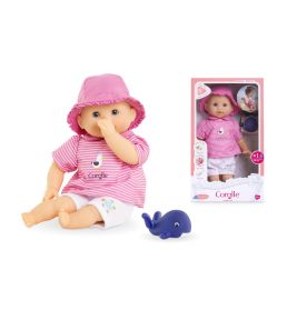 Eine Babypuppe in rosa Kleidung und Mütze sitzt mit einem blauen Wal-Spielzeug neben ihrer Verpackung.