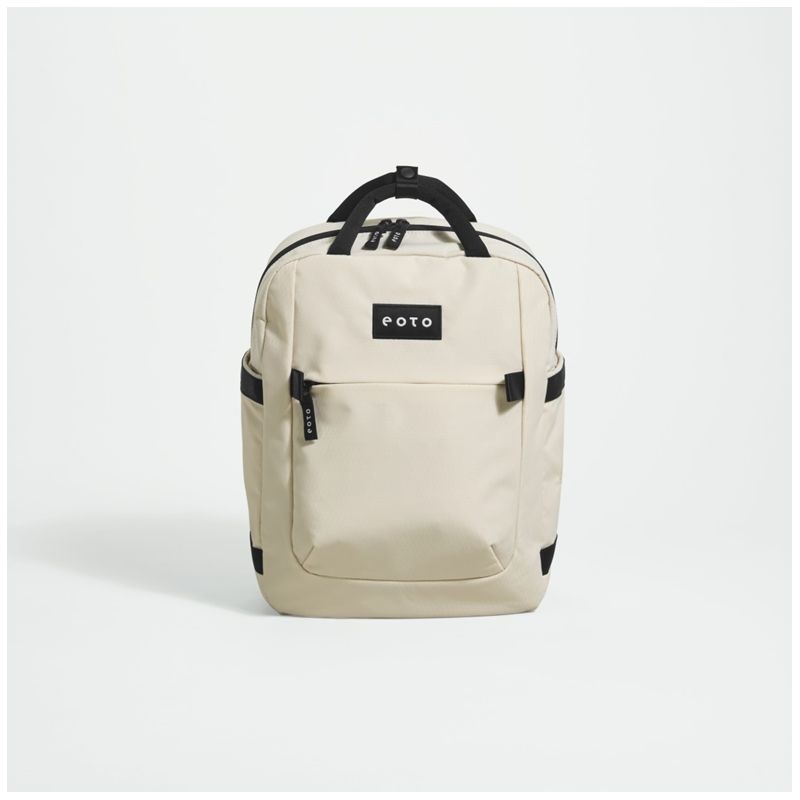 Cremefarbener Rucksack mit schwarzen Akzenten und Fronttasche steht aufrecht vor weißem Hintergrund.