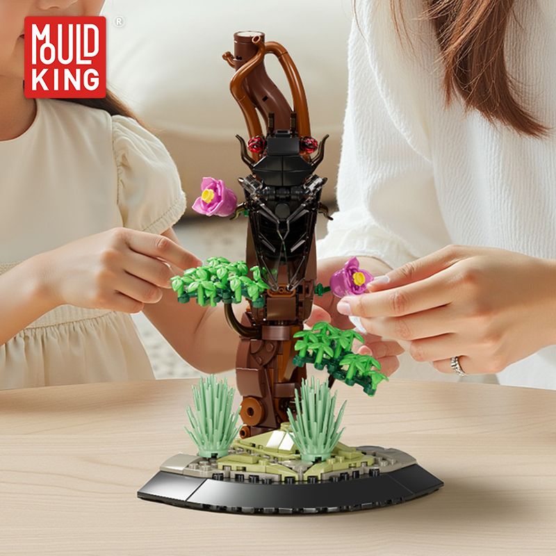 Zwei Personen bauen auf einem Tisch ein LEGO-Fantasiebaum-Modell mit rosa Blüten und grünen Blättern.