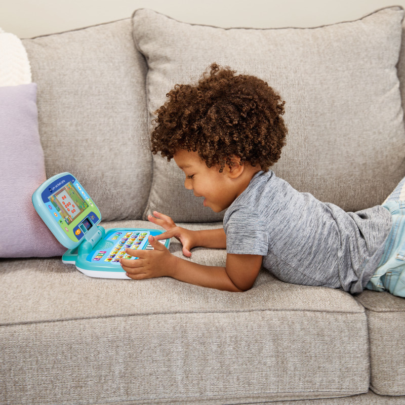 Ein Kind liegt auf dem Sofa und spielt mit einem blauen Lern-Laptop.