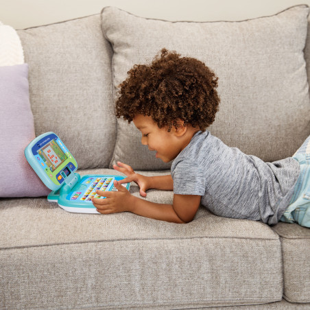 Ein Kind liegt auf dem Sofa und spielt mit einem blauen Lern-Laptop.