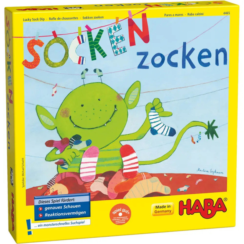 Ein grünes Monster sortiert Socken auf einer bunten Spielebox mit der Aufschrift Socken zocken von HABA. Ein grünes Monster sortiert Socken auf einer bunten Spielebox mit der Aufschrift Socken zocken von HABA.