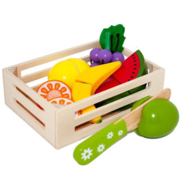 Holzkiste mit Spielzeug-Obst und -Gemüse, davor ein grünes Spielmesser und ein Apfel.