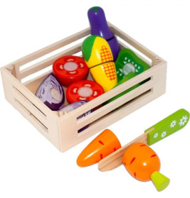 Holzkiste mit buntem Spielzeuggemüse, daneben liegen eine Spielzeugkarotte und ein Messer.