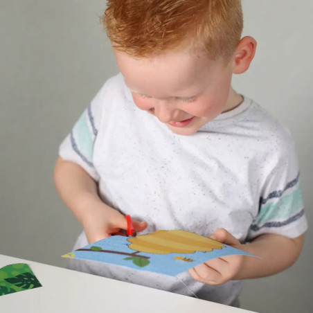 Ein lächelnder Junge schneidet mit roten Scheren buntes Papier an einen weißen Tisch. Ein lächelnder Junge schneidet mit roten Scheren buntes Papier an einen weißen Tisch.