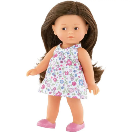 Puppe mit langen braunen Haaren, Blumenkleid und rosa Schuhen steht vor weißem Hintergrund.