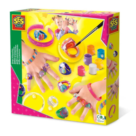 Bastelset mit bunten Ringen, Armbändern, Farbtöpfen und Pinsel auf Gelb, Hände zeigen Schmuck.