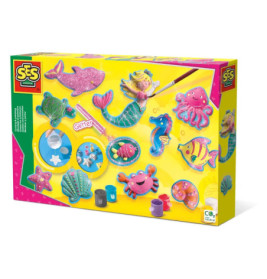 Bunte Bastelbox mit Meerjungfrauen-Motiv, Meerestieren, Farben und Glitzer auf gelbem Hintergrund.