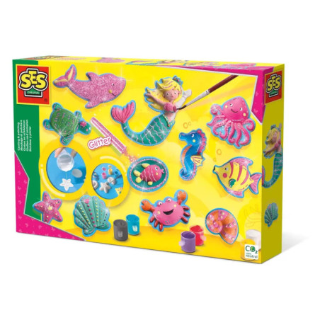 Bunte Bastelbox mit Meerjungfrauen-Motiv, Meerestieren, Farben und Glitzer auf gelbem Hintergrund.