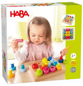 Kleinkind spielt mit bunten Steckspielzeugen auf Holzbrett HABA-Logo und Alter 2+ auf der Verpackung sichtbar.