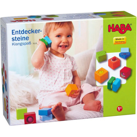 Ein lachendes Baby spielt mit bunten Holzklötzen, daneben steht die HABA Entdeckersteine-Spielbox. Ein lachendes Baby spielt mit bunten Holzklötzen, daneben steht die HABA Entdeckersteine-Spielbox.