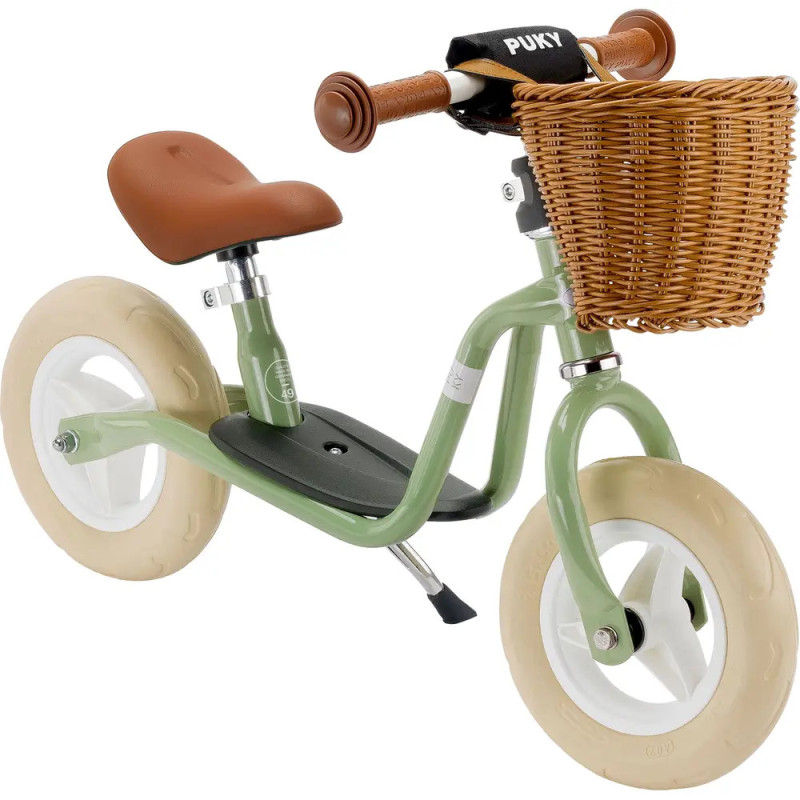 Grünes Laufrad mit cremefarbenen Reifen, braunem Sitz, braunen Griffen und einem Weidenkorb am Lenker.