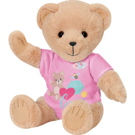 Ein hellbrauner Teddybär im rosa Shirt mit Bären- und Herzmotiv sitzt und winkt.