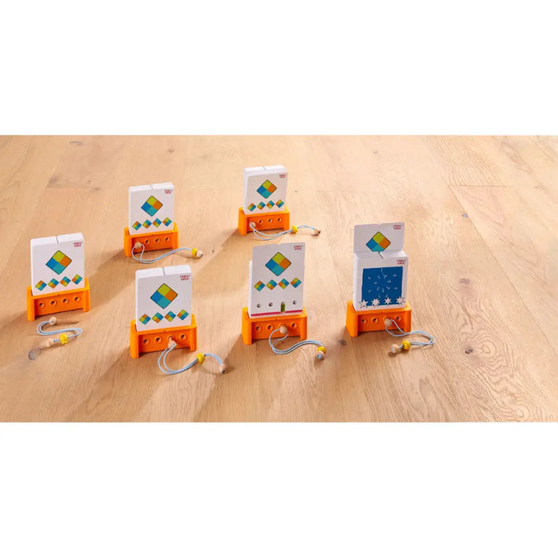 Sechs Lernspielkarten in orangefarbenen Haltern mit angeschlossenen Ohrhörern auf hellem Holzfußboden.