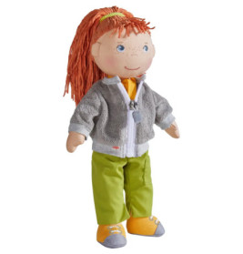 Stoffpuppe mit roten Garnhaaren, grauer Jacke, grüner Hose und gelben Schuhen steht aufrecht.