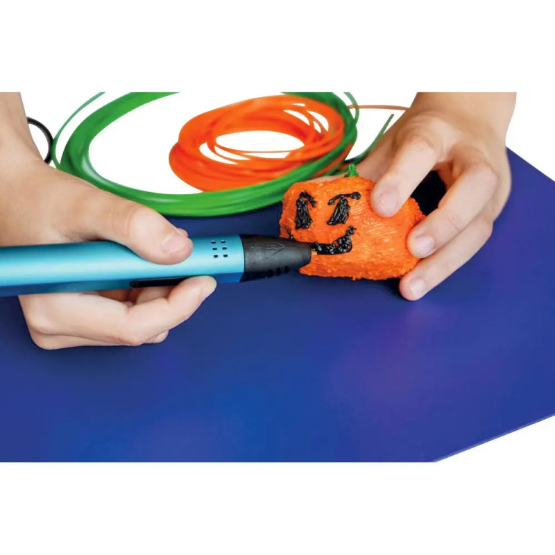 Ein Kind zeichnet mit einem blauen 3D-Stift ein schwarzes Smiley auf einen orangefarbenen Gegenstand, Filament im Hintergrund.