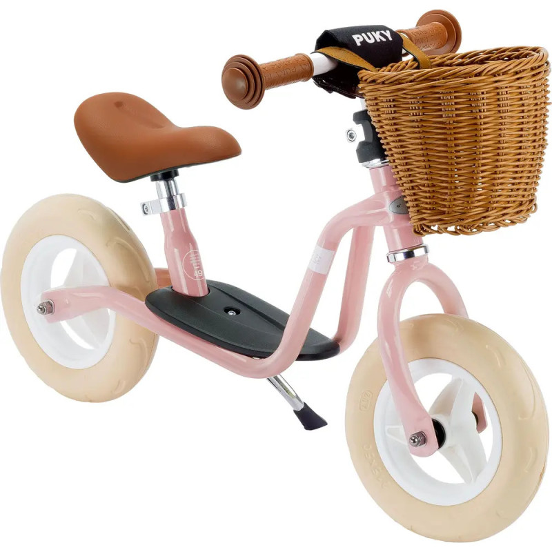 Pinkes Laufrad mit cremefarbenen Reifen, braunem Sattel, braunen Griffen und Weidenkorb vorne.