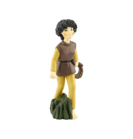 Plastikfigur einer Person mit Locken, gelber Hose, brauner Tunika auf grün strukturiertem Untergrund.