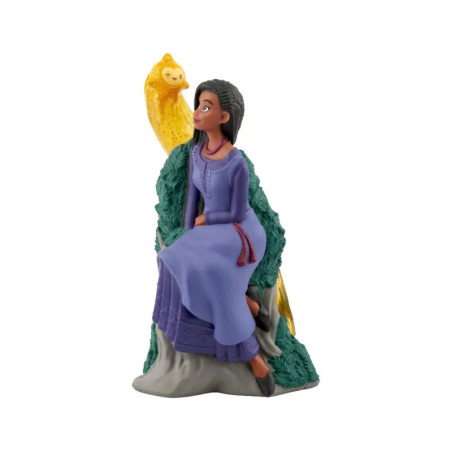 Eine Figurine einer Frau im lila Kleid sitzt neben einem gelben Vogel auf einem grünen Baumstamm. Eine Figurine einer Frau im lila Kleid sitzt neben einem gelben Vogel auf einem grünen Baumstamm.