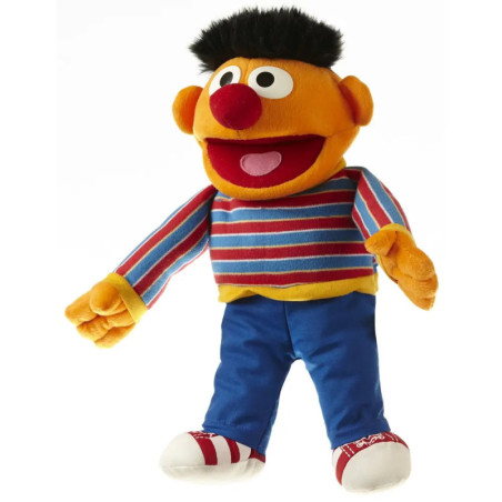 Ein Plüschtier mit oranger Haut, schwarzen Haaren, gestreiftem Shirt, blauer Hose und Sneakern lächelt breit.