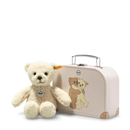 Ein beiger Teddybär sitzt neben einem weißen Koffer mit einer Illustration von zwei umarmenden Bären.
