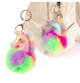 Zwei Einhorn-Schlüsselanhänger mit Regenbogenmähnen und bunten Pompons hängen an einer beigefarbenen Tasche.