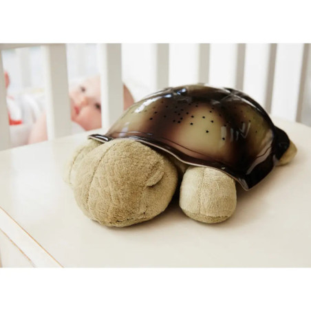 Ein Plüsch-Schildkröten-Nachtlicht steht auf einem Tisch neben einem Babybett mit einem Baby darin.