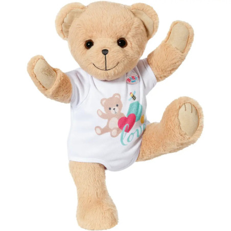Hellbrauner Teddy mit weißem Shirt und bunten Motiven, steht auf einem Bein und hebt beide Arme.