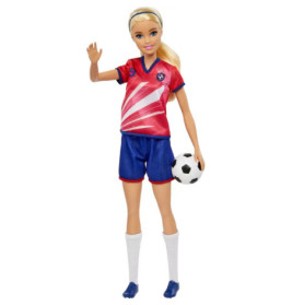 Barbie-Puppe im rot-blauen Fußballtrikot hält einen Ball und winkt mit der linken Hand.