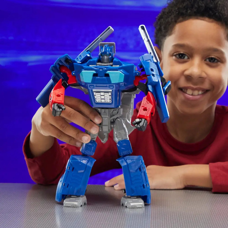 Lächelnder Junge im roten Shirt hält eine blau-rote Roboterfigur am Tisch.