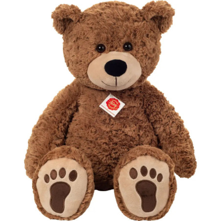 Großer, flauschiger brauner Teddybär mit einem Anhänger um den Hals sitzt aufrecht und schaut nach vorne.