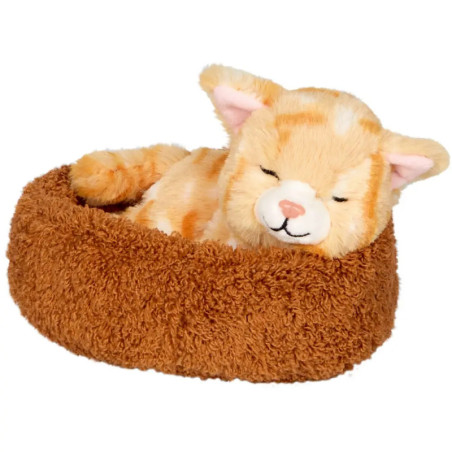 Ein orangefarbenes Kuscheltier in Katzenform schläft in einem runden, braunen, flauschigen Tierbett.