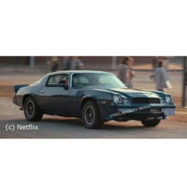 Ein blauer Oldtimer fährt auf einer Straße, im Hintergrund sind unscharfe Personen zu sehen.