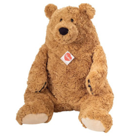 Großer brauner Teddybär mit lockigem Fell, beigen Pfoten und rotem Etikett sitzt aufrecht.