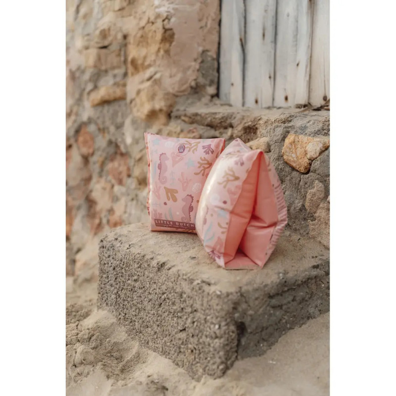 Zwei pinke Schwimmflügel mit Strandmotiv liegen auf einer Steinstufe an einer verwitterten Wand.